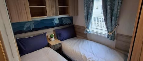 A small, cozy room with two beds, a small table with a plant, and a window with curtains.
