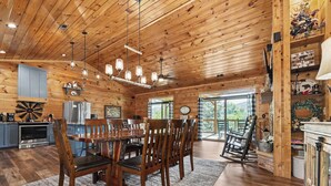 A rustic cabin interior with a dining table, chairs, kitchen area, and a rocking chair. - New Cabin w/view|Hot tub|Himalayan Salt Room|Walk to Downtown Gatlnburg (GATLINBURG)
