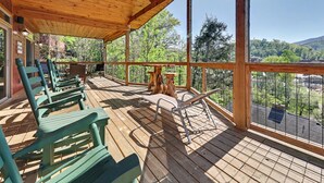 A wooden deck with chairs and a table, overlooking a forested area. - New Cabin w/view|Hot tub|Himalayan Salt Room|Walk to Downtown Gatlnburg (GATLINBURG)