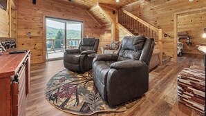A wooden cabin interior with a fireplace, a sofa, a dining table, and a staircase. - New Cabin w/view|Hot tub|Himalayan Salt Room|Walk to Downtown Gatlnburg (GATLINBURG)