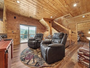 A wooden cabin interior with a fireplace, a sofa, a dining table, and a staircase. - New Cabin w/view|Hot tub|Himalayan Salt Room|Walk to Downtown Gatlnburg (GATLINBURG)