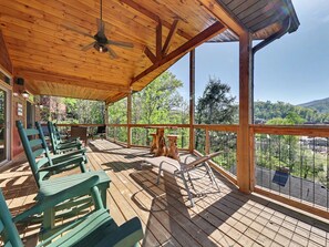 A wooden deck with chairs and a table, overlooking a forested area. - New Cabin w/view|Hot tub|Himalayan Salt Room|Walk to Downtown Gatlnburg (GATLINBURG)