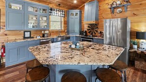 A kitchen with granite countertops, wooden cabinets, and a central island with stools. - New Cabin w/view|Hot tub|Himalayan Salt Room|Walk to Downtown Gatlnburg (GATLINBURG)