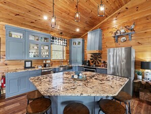A kitchen with granite countertops, wooden cabinets, and a central island with stools. - New Cabin w/view|Hot tub|Himalayan Salt Room|Walk to Downtown Gatlnburg (GATLINBURG)