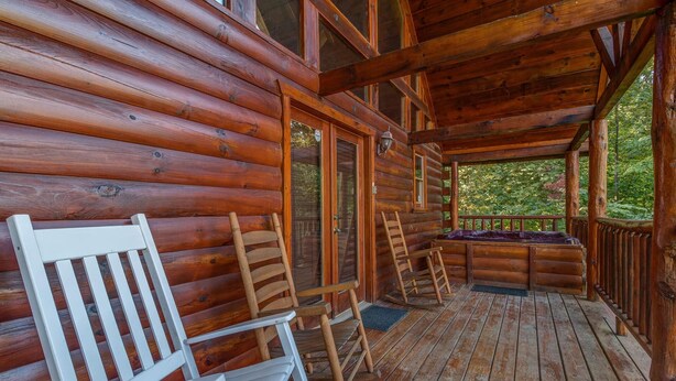 Eine Blockhütte mit Veranda, Holzstühlen, einer Bank und Blick auf den umliegenden Wald.