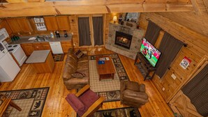 Ein gemütliches Blockhaus-Interieur mit Kamin aus Stein, Holzmöbeln, einem Fernseher und einer Küchenzeile.