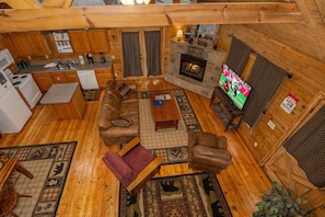 A cozy cabin interior with a stone fireplace, wooden furniture, a television, and a kitchen area. - Hot Tub | Fireplace | Multicade | Mountain Views (Sevierville)