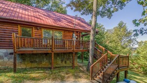 Eine Blockhütte mit Steinunterbau, einer Holzterrasse und einem Metalldach.