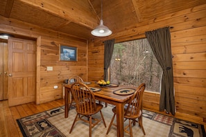 A wooden cabin interior with a dining table, chairs, a hanging light fixture, and a window with curtains. - Hot Tub | Fireplace | Multicade | Mountain Views (Sevierville)