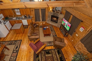 Ein gemütliches Blockhaus-Interieur mit Kamin aus Stein, Holzmöbeln, einem Fernseher und einer Küchenzeile.