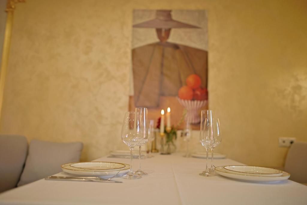 A dining table set with plates, cutlery, and glasses, with a painting and candles in the background.