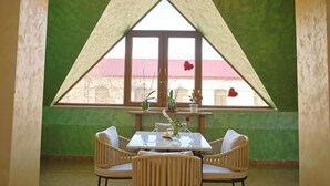 A dining area with a table and chairs, a window with a view of buildings, and a green wall. - Passage Hotel Restaurant (Goris)