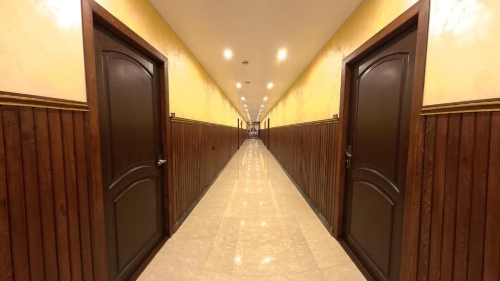A corridor with wooden paneling on the walls and a marble floor, leading to a set of double doors.