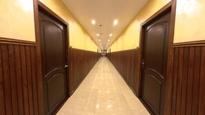 A corridor with wooden paneling on the walls and a marble floor, leading to a set of double doors.