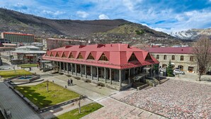 A building with a red roof, a courtyard with a fountain, and a mountainous backdrop. - Passage Hotel Restaurant (Goris)