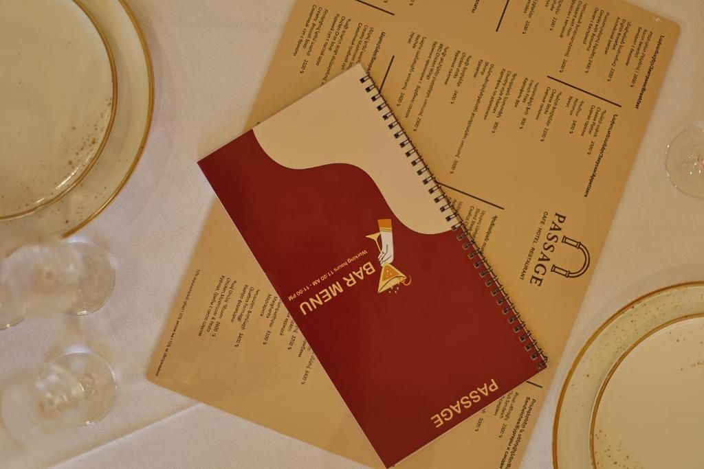 Um menu com capa vermelha e texto, colocado sobre uma mesa com toalha branca e copos de vidro transparentes.