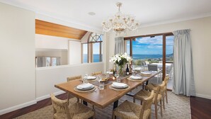 Ein Esszimmer mit einem Holztisch, gedeckt für sechs Personen, Korbstühle, einer Kristallleuchtre und Meerblick durch große Fenster.