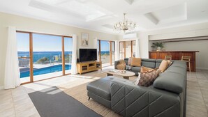 Ein modernes Wohnzimmer mit einem großen grauen Sofa, einem Fernseher und Blick auf einen Swimmingpool.