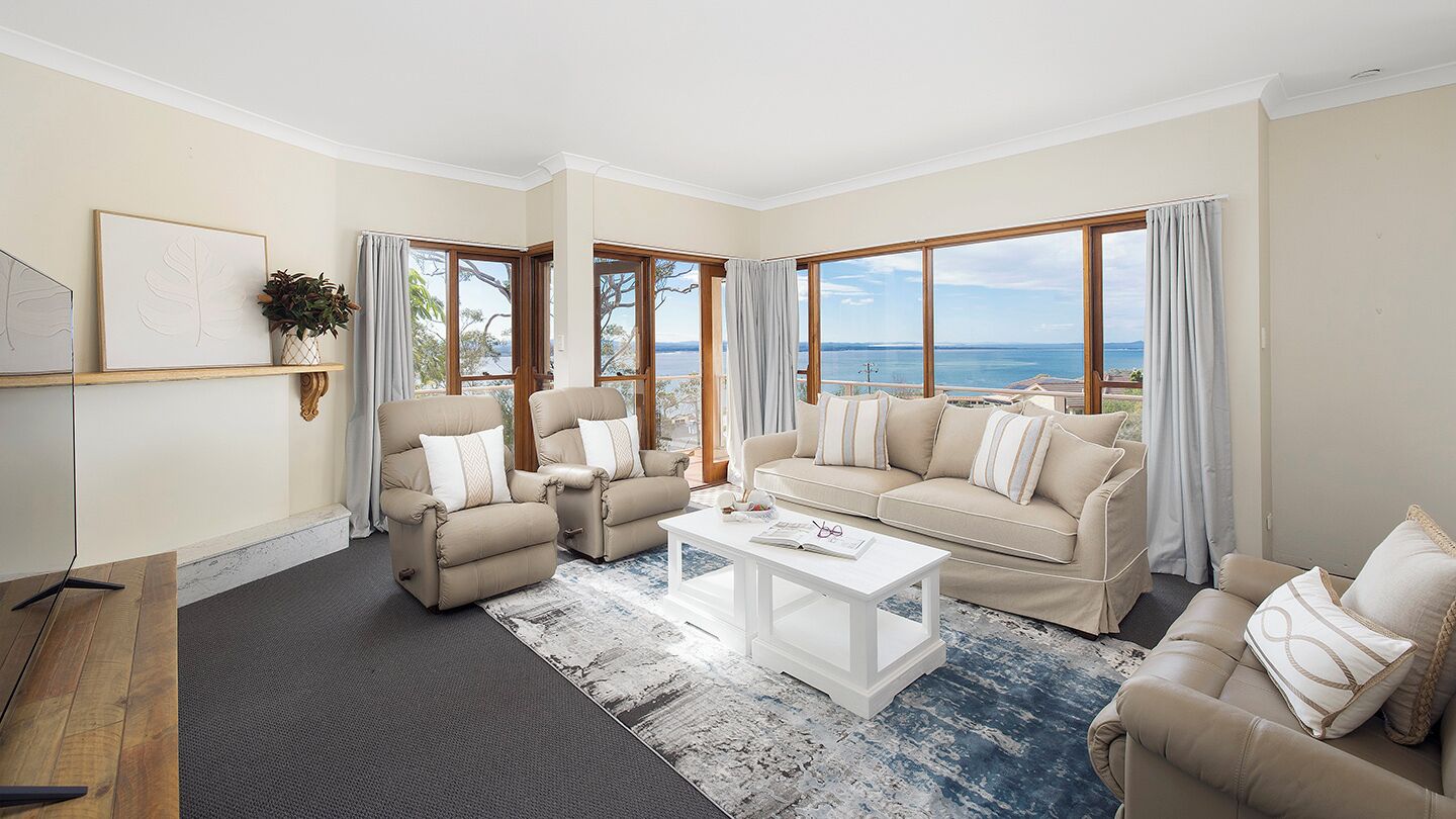 A spacious living room with a large window offering a view of the sea, a beige sofa set, and a coffee table.
