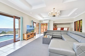 A modern living room with a large gray sectional sofa, a flat-screen TV, and a pool view.