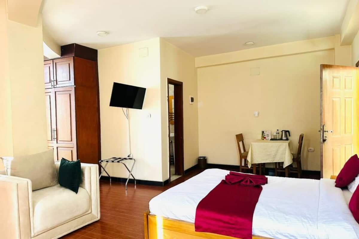 Una habitación de hotel con cama, sofá, televisor, mesa de comedor y puerta.