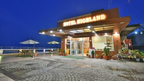 Ein Hotel Eingang mit einem Schild mit der Aufschrift 'HOTEL HIGHLAND', Blumentöpfen und Außenbestuhlung.