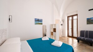 A hotel room with a bed, a blue bedspread, a sofa, a mirror, and a door leading to a balcony. - Apartment 'L'angolo Del Teatro' with Private Terrace and Air Conditioning (Galatone)