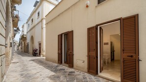 A narrow cobblestone street with buildings on either side, featuring open wooden shutters and a parked motorcycle. - Apartment 'L'angolo Del Teatro' with Private Terrace and Air Conditioning (Galatone)