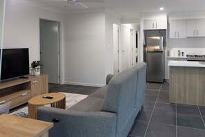 Un salon moderne avec un canapé, un téléviseur, un meuble en bois et une petite table ronde.