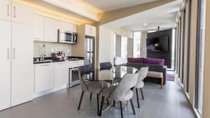 Une cuisine moderne avec des meubles blancs, des appareils en acier inoxydable et un coin repas comprenant une table et des chaises en verre.