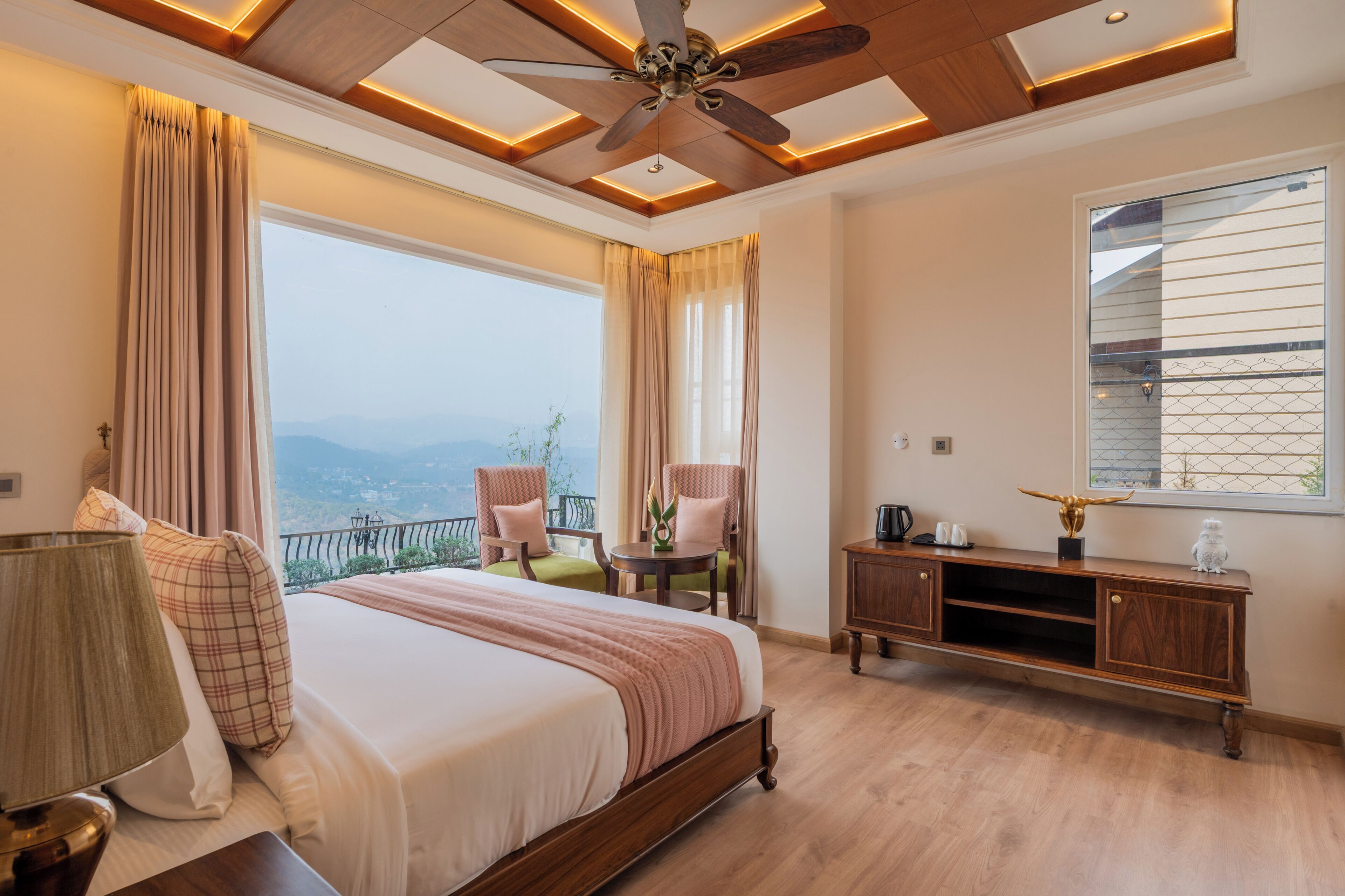 Een slaapkamer met een bed, een plafondventilator, uitzicht op de bergen en een balkon met stoelen.