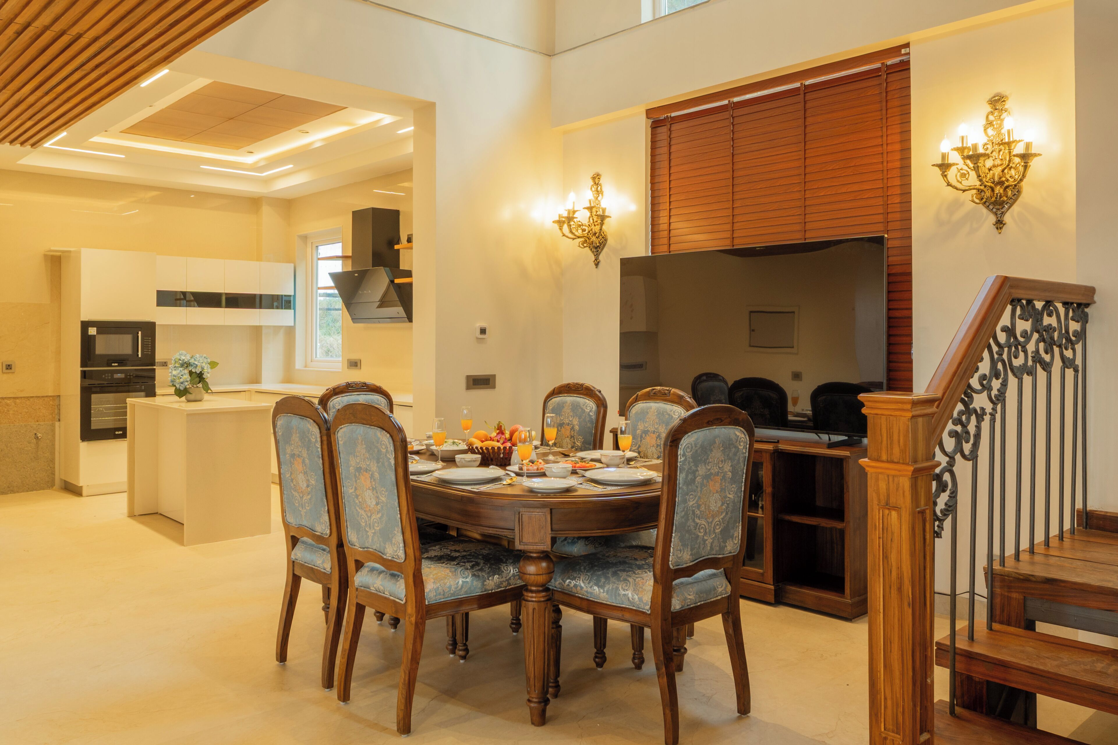 A dining area with a round table, six chairs, and a kitchen in the background.