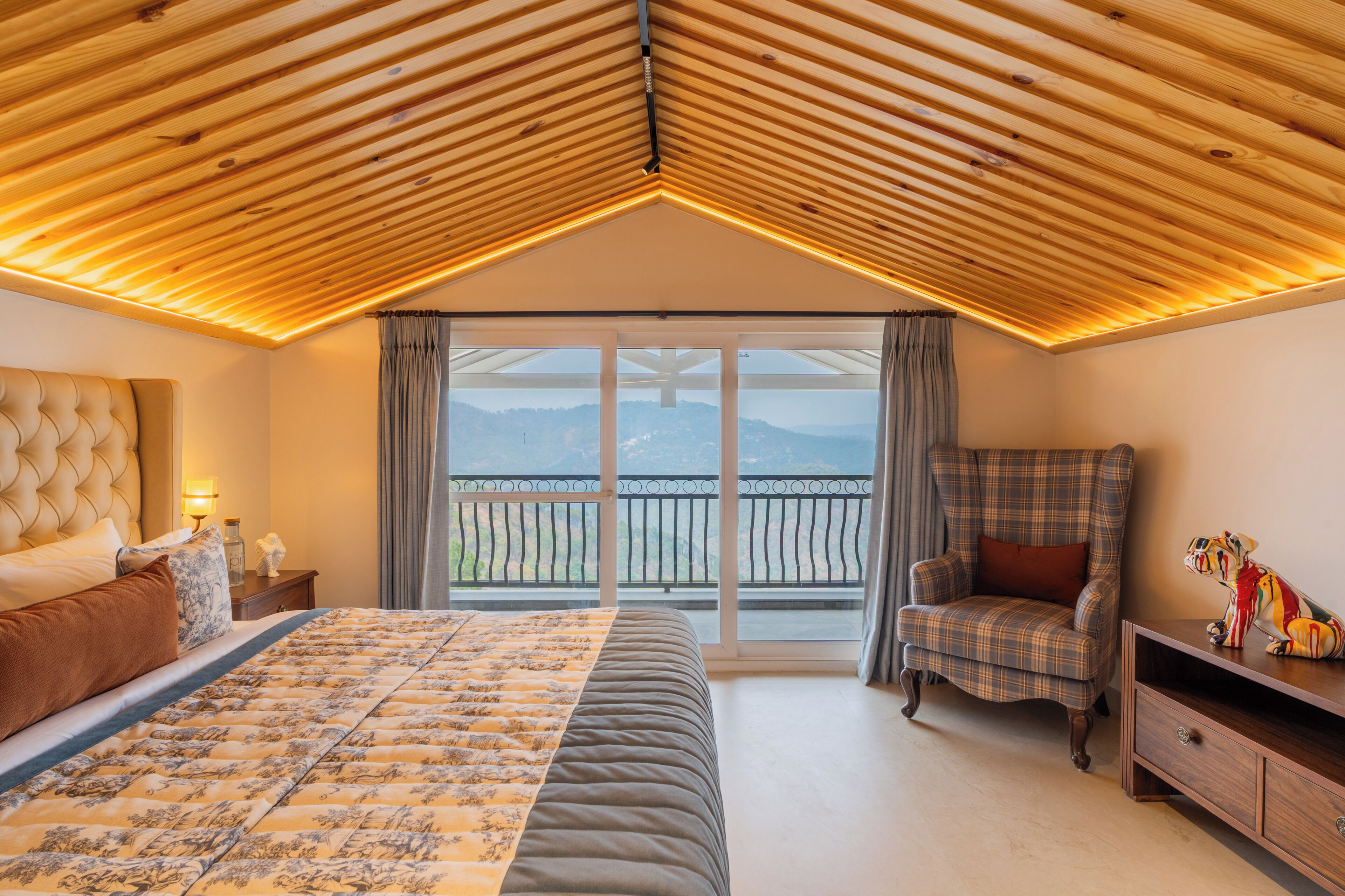 A bedroom with a large bed, a chair, a nightstand, and a view of the outdoors.