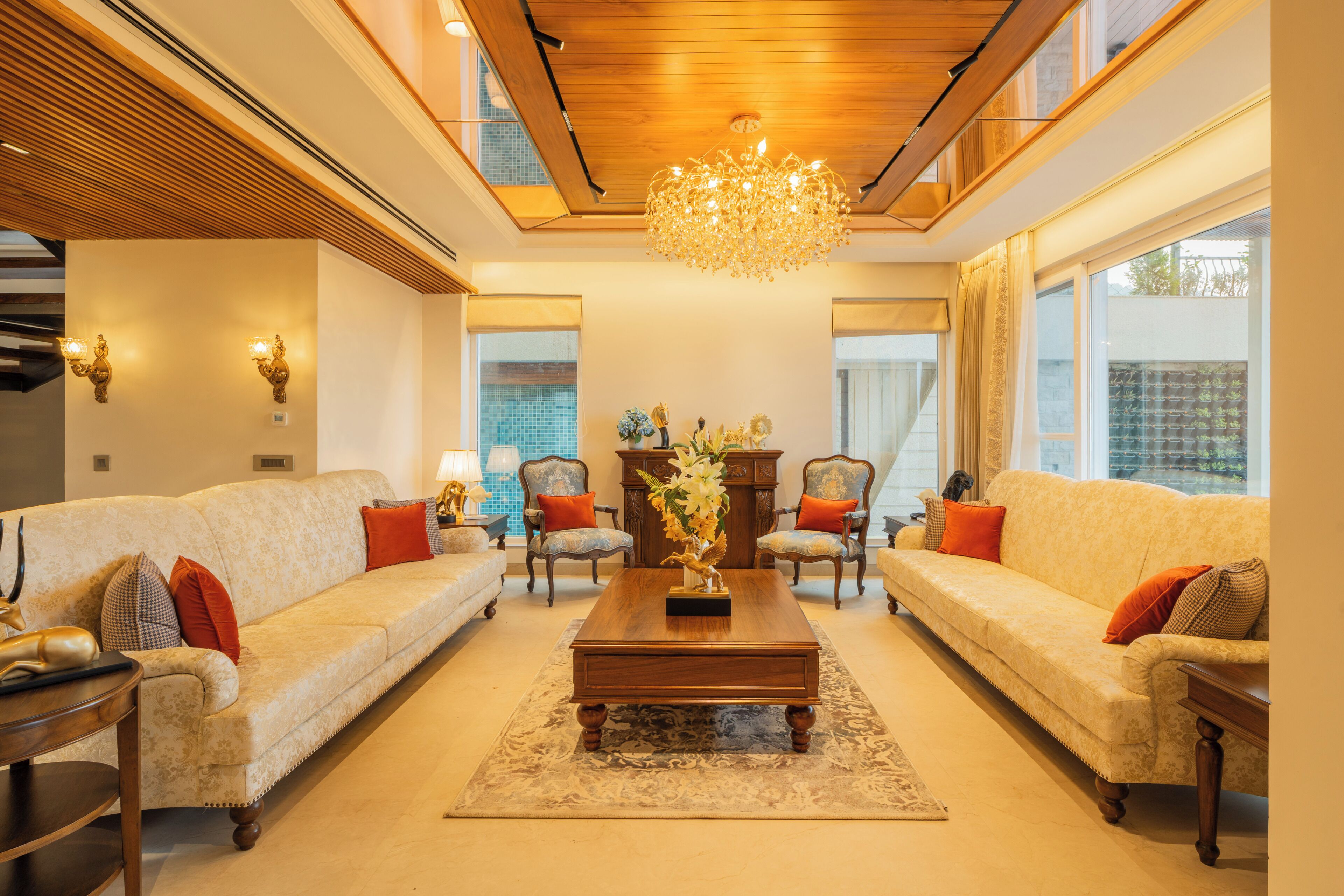 A spacious living room with a wooden ceiling, a central coffee table, two sofas with cushions, and a chandelier.