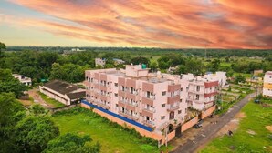 A multi-story residential building with a flat roof, surrounded by greenery and a clear sky. - Somani Inn (Jhargram)