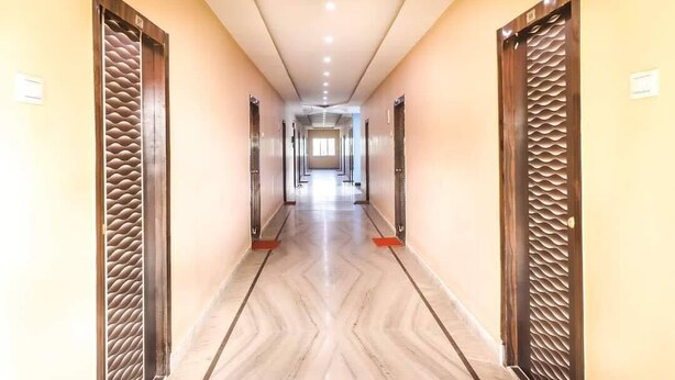 A long, narrow hallway with a marble floor and wooden doors with textured panels. - Somani Inn (Jhargram)