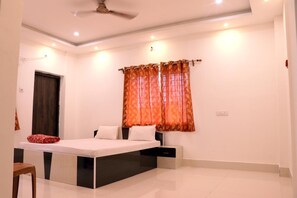 A bedroom with a bed, a chair, a bedside table, a wardrobe, and a window with curtains. - Somani Inn (Jhargram)