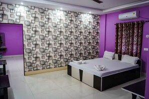 A bedroom with a patterned wall, a bed, a table, and an air conditioning unit. - Somani Inn (Jhargram)