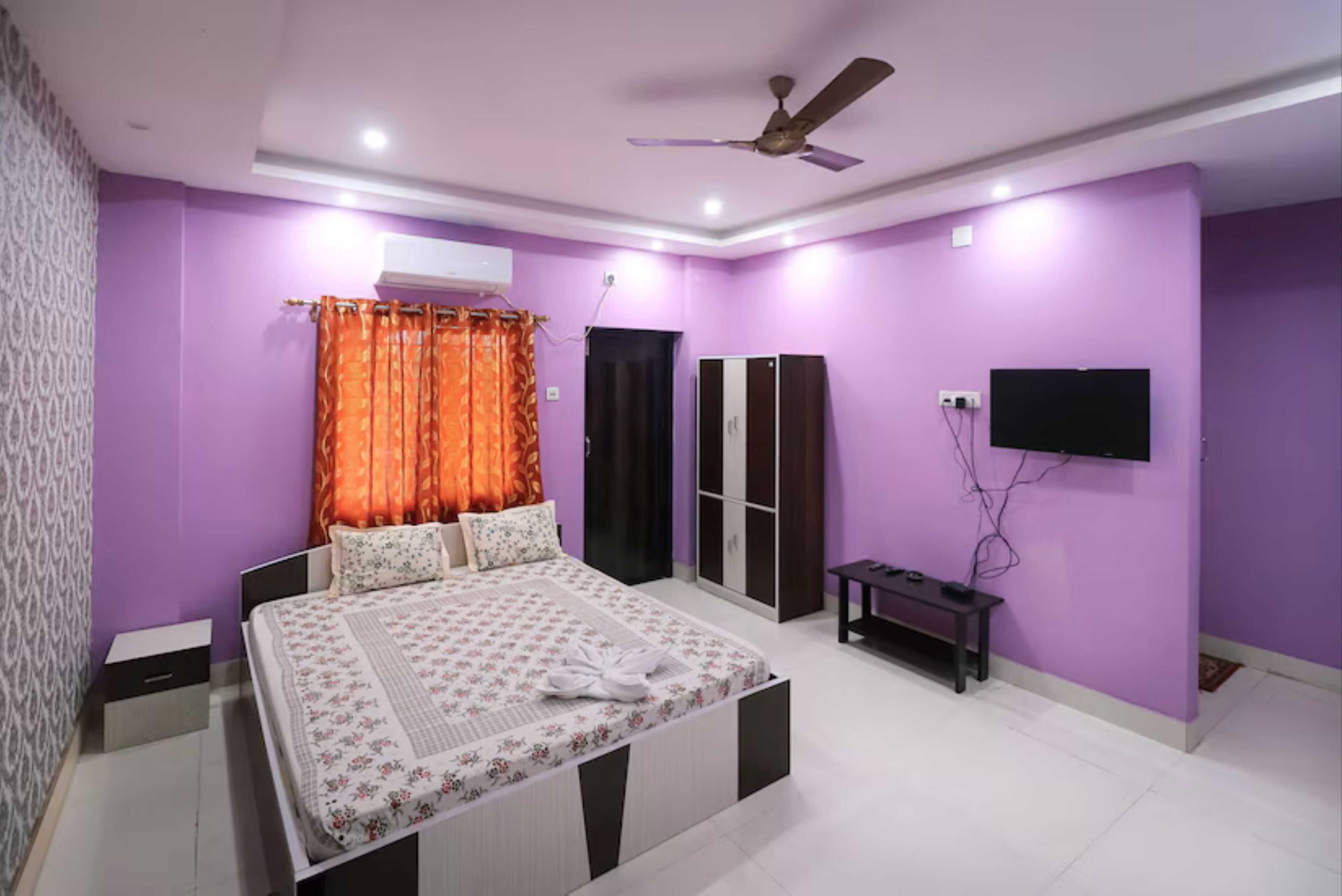A bedroom with a bed, a wardrobe, a TV, and a ceiling fan.