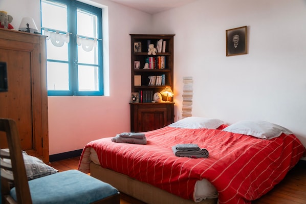 A bedroom with a bed, a wooden wardrobe, a bookshelf, and a window.