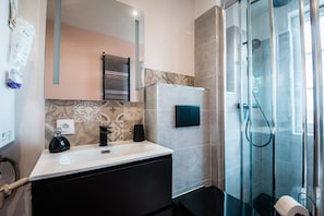 A bathroom with a sink, mirror, towel dispenser, and glass shower enclosure.