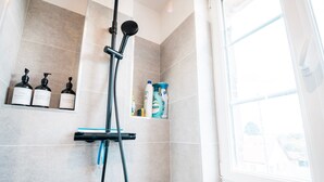 Una doccia con soffione a mano e dispenser con prodotti da bagno su uno scaffale.