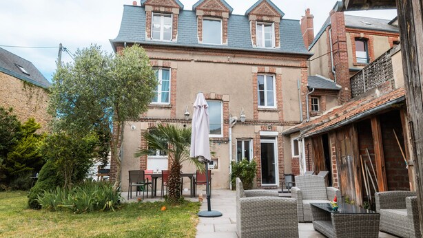 Una casa in mattoni con patio, mobili da esterno e un piccolo giardino.