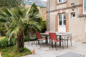 An outdoor patio with a table and chairs, surrounded by greenery and a brick building.