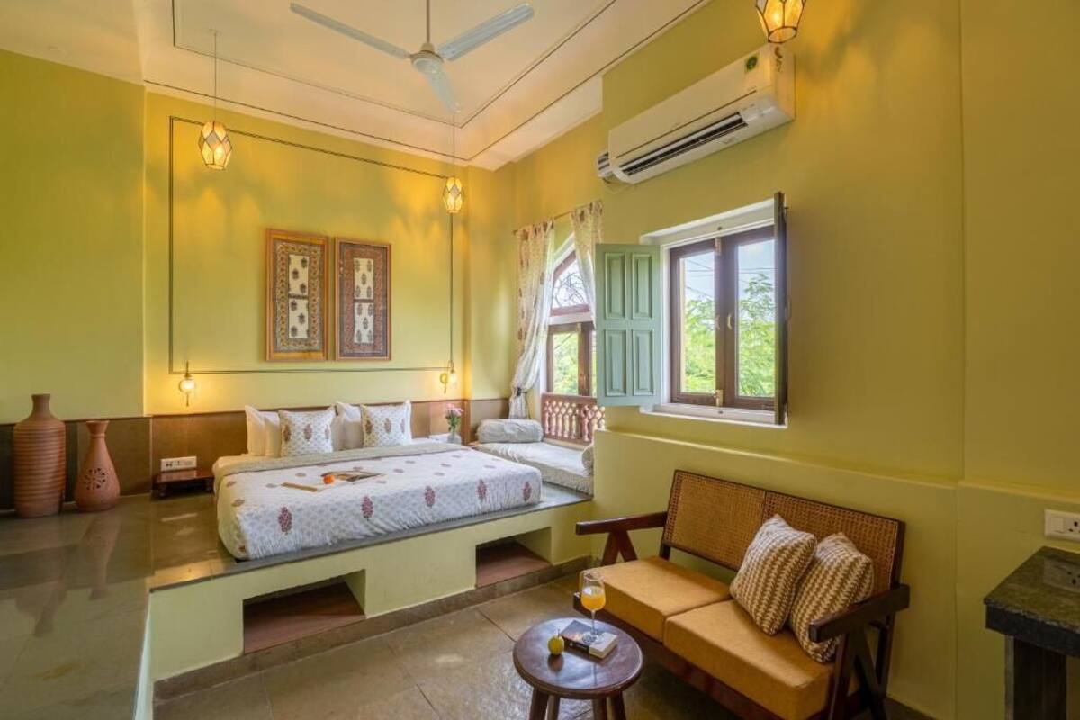 Una habitación con cama, sofá, una mesita, ventilador de techo y ventana con cortinas.