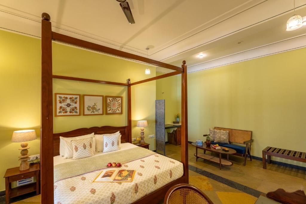 A four-poster bed with a floral bedspread, bedside lamps, and a small table with a book and a plant.