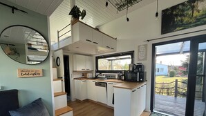 A compact kitchen with white cabinets, a wooden countertop, and a view of the outdoors through a large window. - Cozy Tiny House "Spree-Maus" Family-friendly - only 50m to the Spree (Grünheide (Mark))