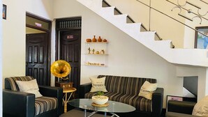 A living room with a sofa set, a glass coffee table, a gramophone, and a staircase.