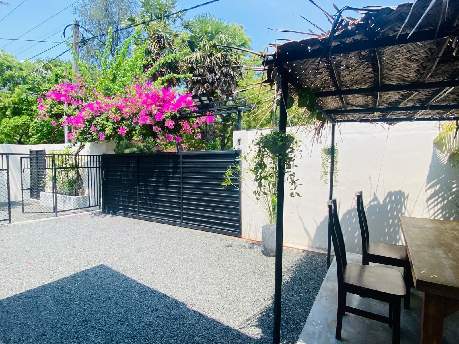 Un patio con mesa y sillas, un portón negro y una pared con un cerrojo negro.