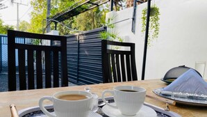A table with two white cups of coffee on a tray, a black chair, and a grill in the background.